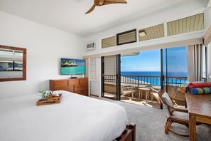 A hotel room with a bed, a TV, a wooden dresser, a balcony with a view of the ocean, and a dining area with chairs and a table. - Kapalua Ridge | Ocean View 5 BR, Sleeps 18 | Car Incl. w/ 6+ Nights | KRV ML-2513 by KBM (Lahaina)