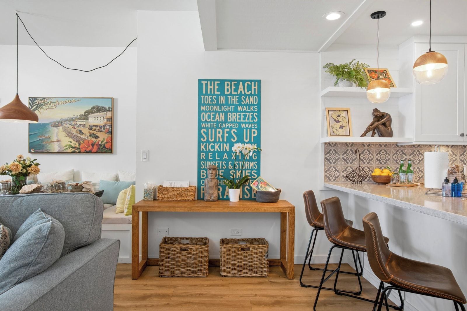 Una sala de estar moderna con un sofá, una mesa de madera con cestas, y una zona de cocina con taburetes de bar.