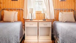 A room with two beds, wooden walls, and a window with curtains. - Bixby Cove Cabin #1 (Porum)