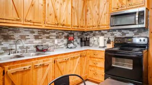 A kitchen with wooden cabinets, a microwave, a stove, and a tiled backsplash. - Bixby Cove Cabin #1 (Porum)