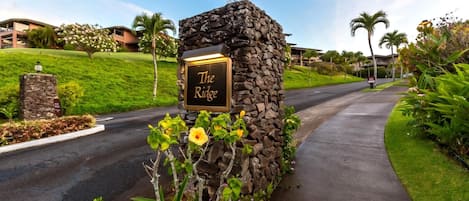 Un panneau en pierre sur lequel est inscrit le mot « The Ridge », entouré de verdure et bordé d’un chemin pavé.