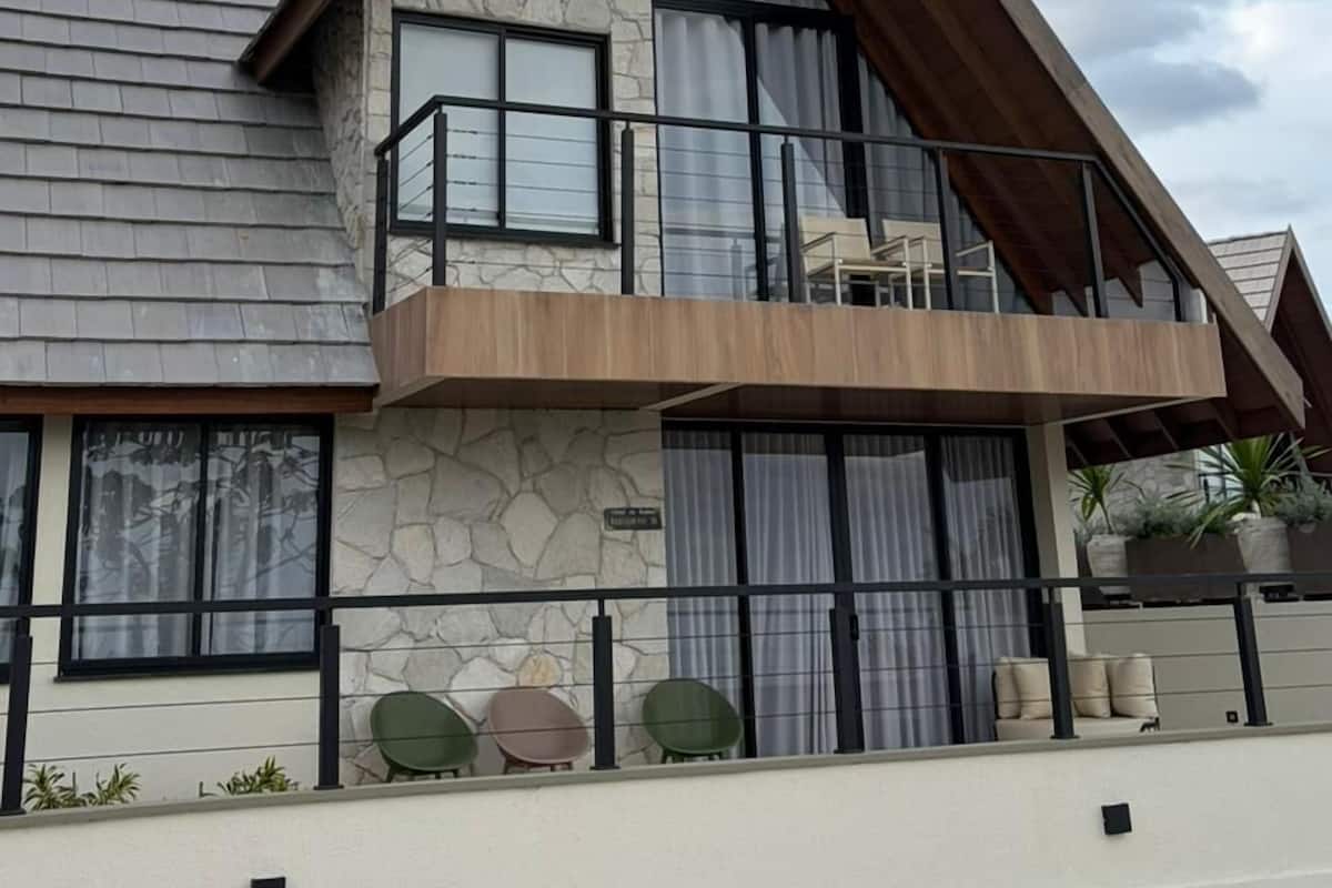A modern two-story house with a stone facade, large windows, and a balcony.
