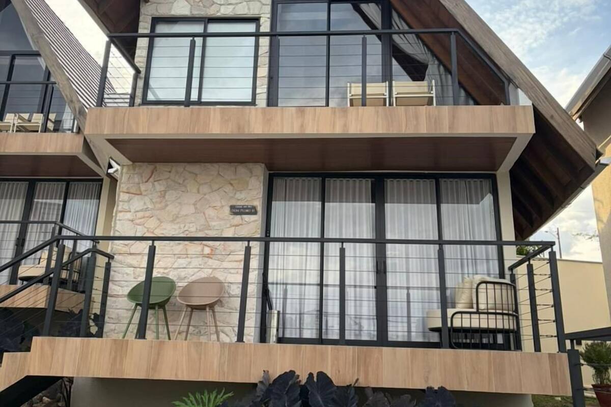A two-story building with a stone facade, large windows, and a balcony with outdoor seating.