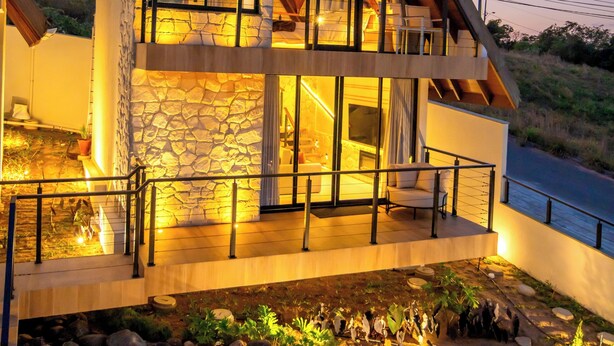 A two-story house with a stone facade, large windows, and a balcony. - Villa Real Chalés (Viçosa do Ceará)