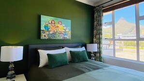 Une chambre avec un grand lit, des murs verts, un tableau au-dessus du lit et une vue sur une montagne par la fenêtre.