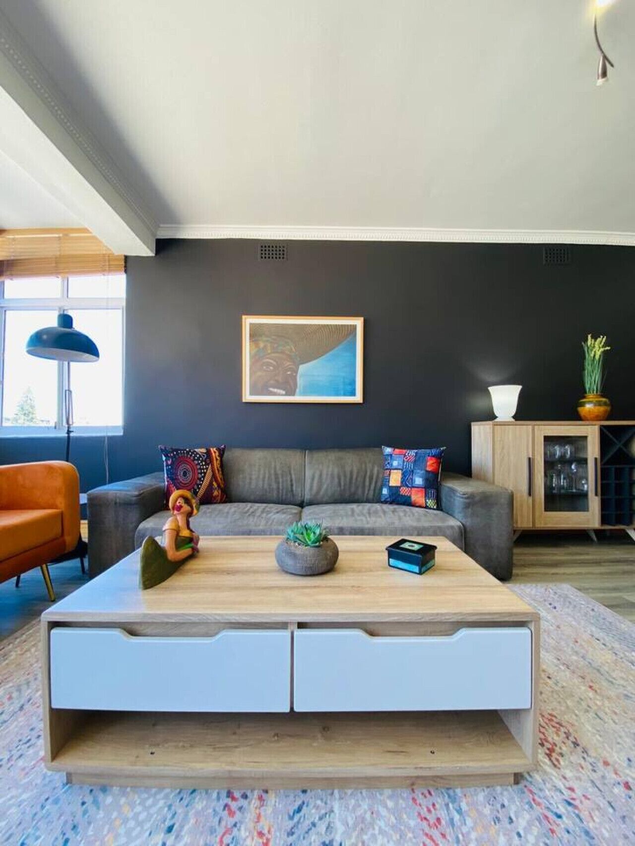 A modern living room with a grey sofa, a wooden coffee table, and a framed artwork on the wall.