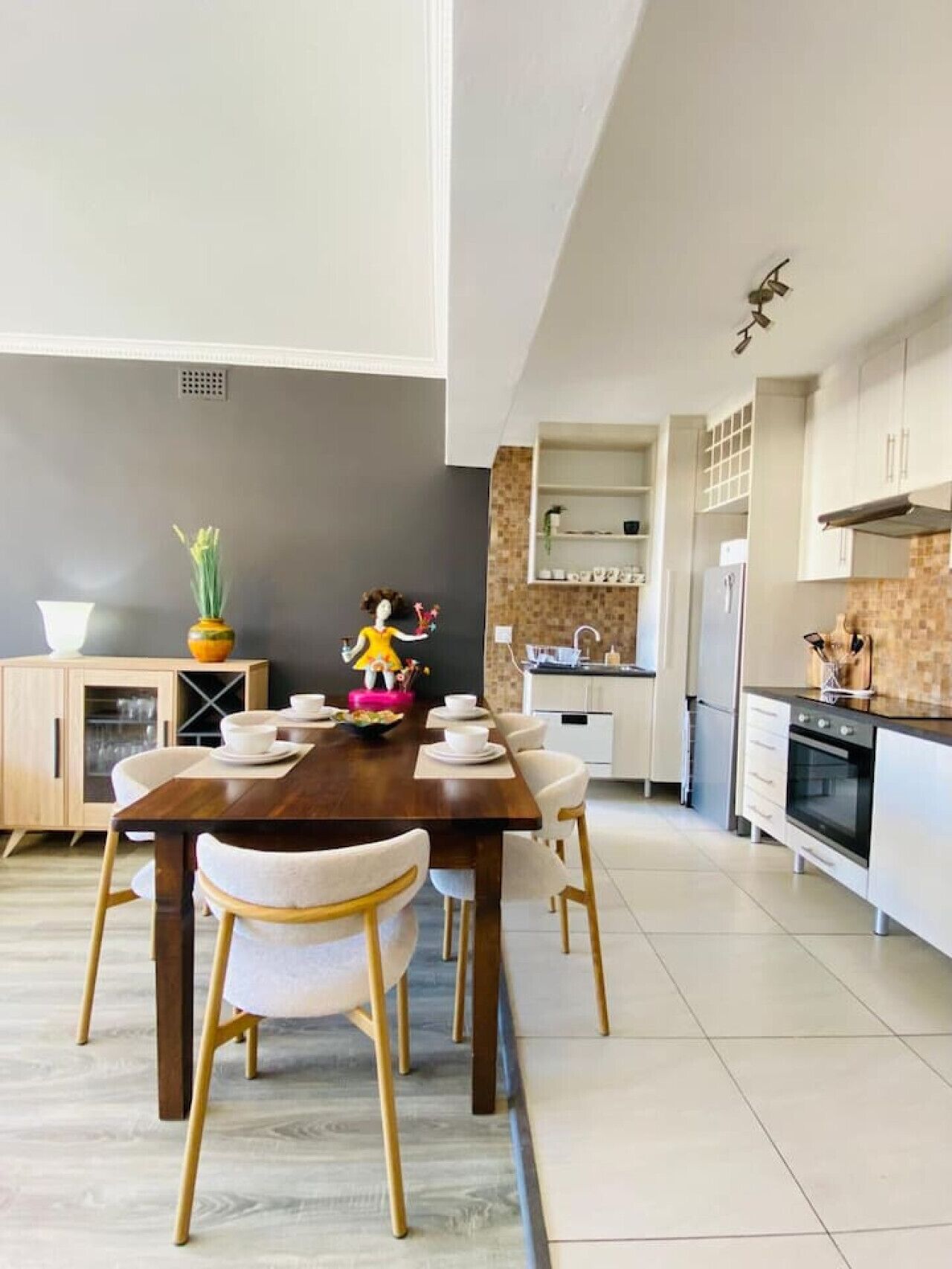 Una cocina moderna con armarios blancos, una mesa de comedor de madera y una figura decorativa.