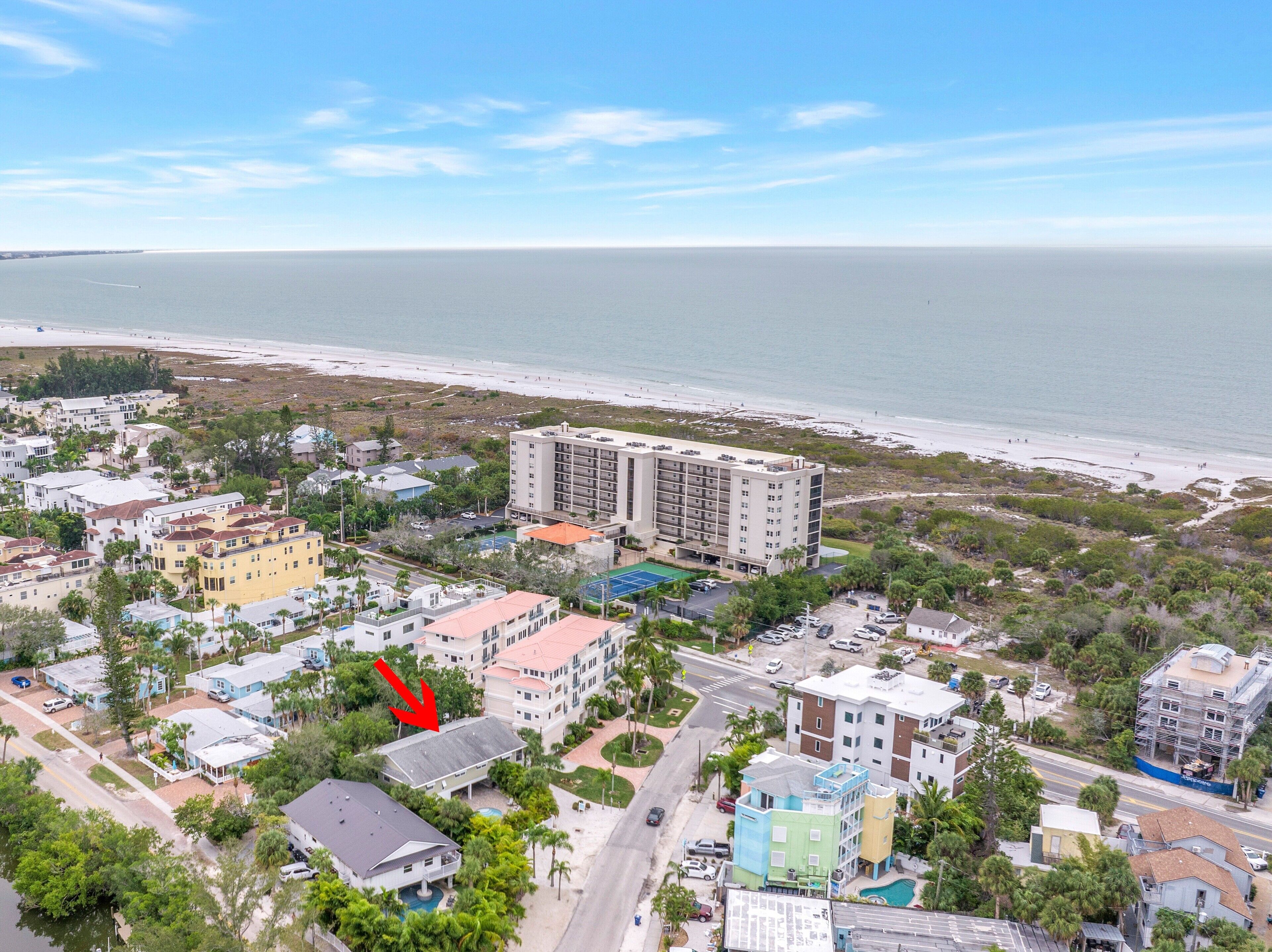 An aerial view of a coastal area with buildings, a beach, and a road.