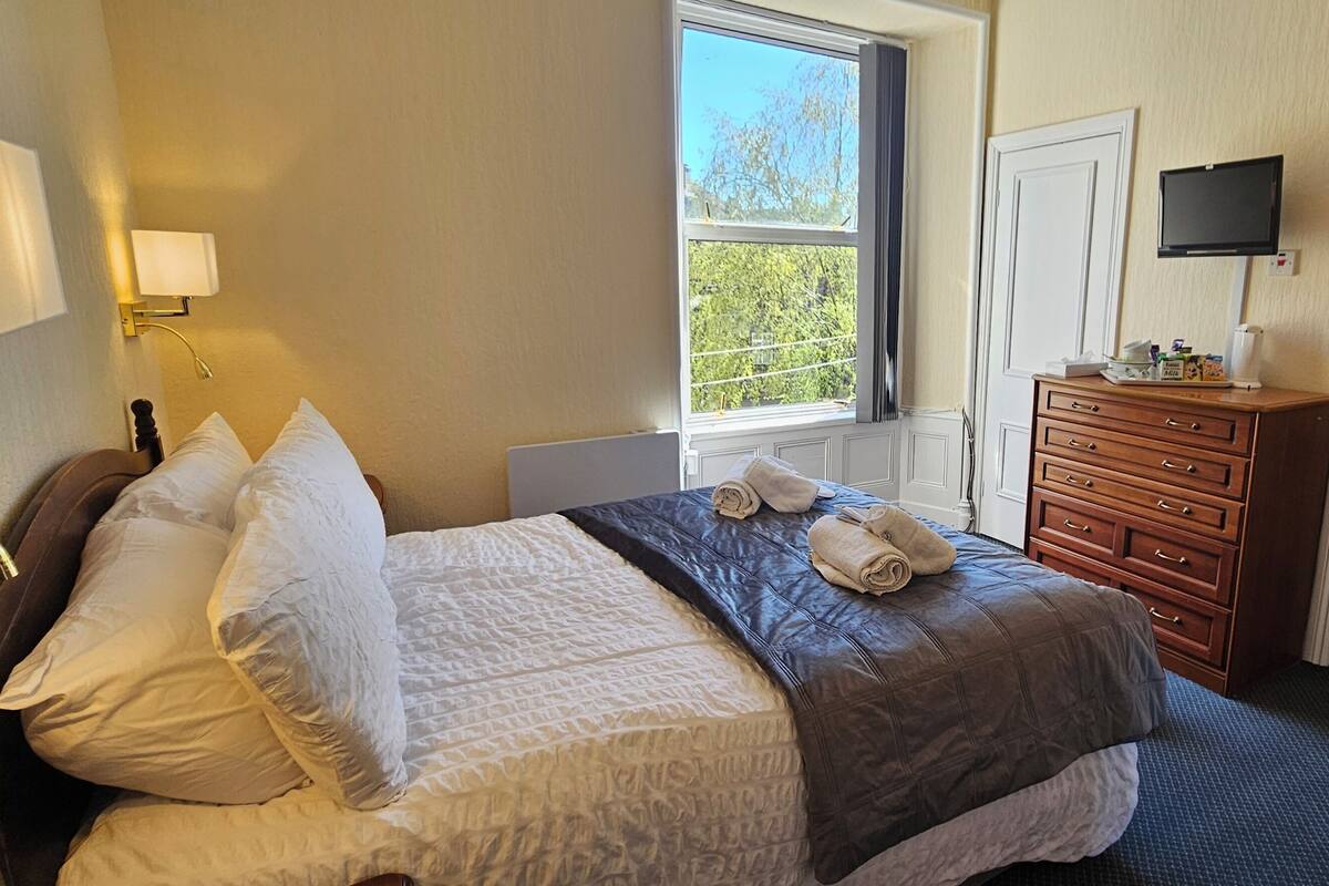 A bedroom with a bed, bedside lamps, a dresser, a TV, and a bathroom with a sink and toilet.
