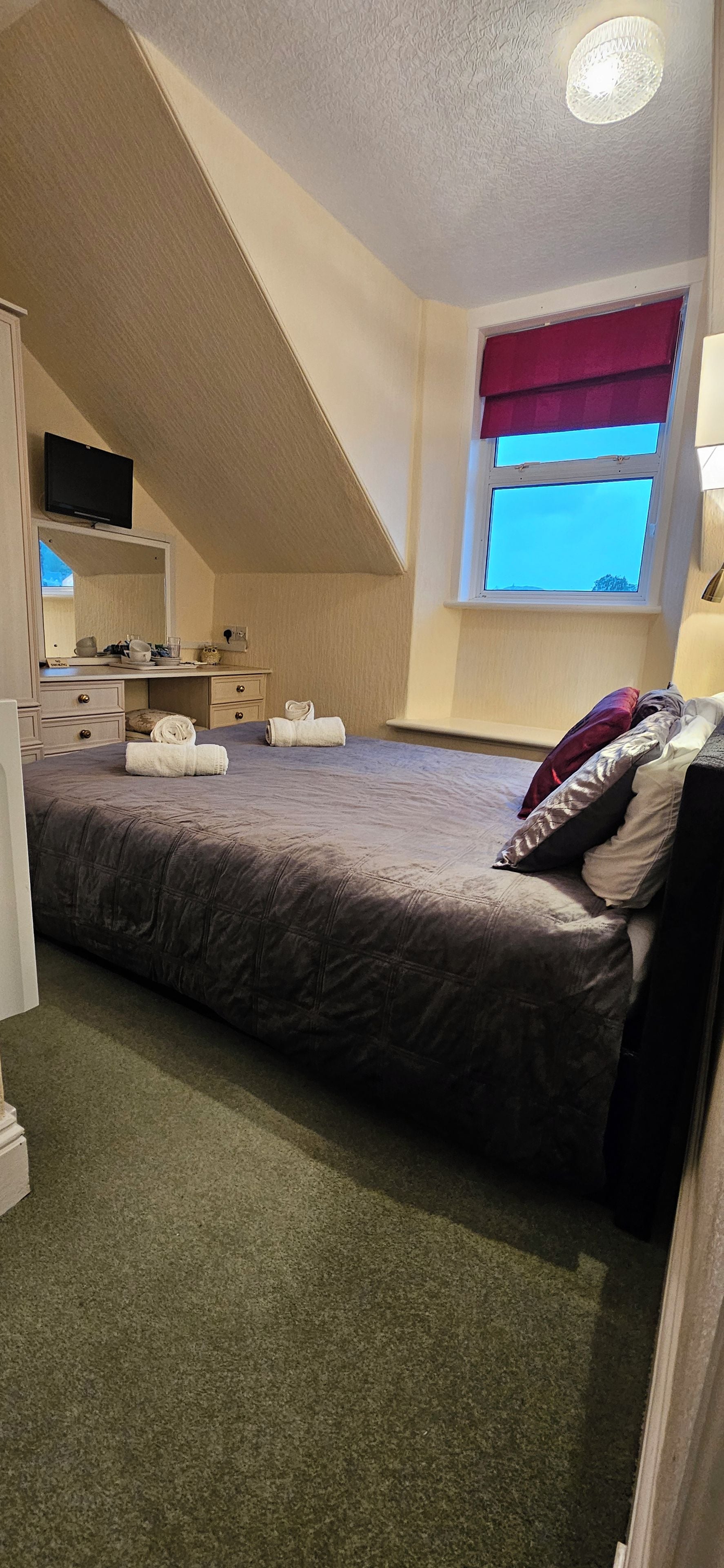 A bedroom with a bed, a desk, a chair, a window, and a television.