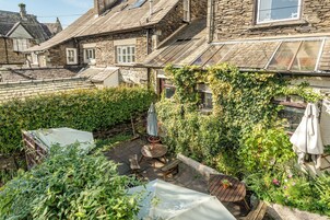 A stone building with a sloped roof, a wooden deck with outdoor furniture, and a garden area with various plants and flowers.