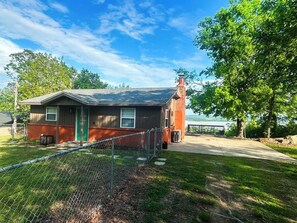 A small house with a brick chimney, a green door, and a fenced yard. - Million-Dollar Lake View + Hot Tub Retreat! (Crowder)