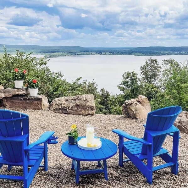 A seating area with two blue chairs and a small table, overlooking a lake with a distant view of hills. - Million-Dollar Lake View + Hot Tub Retreat! (Crowder)