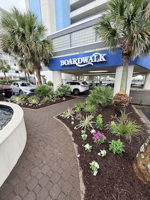 A Boardwalk building with a paved walkway, palm trees, and landscaped flower beds. - The Soaring Seahaven (Myrtle Beach)