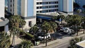 Un hotel de varios pisos con diseño moderno, que presenta un atrio central y un estacionamiento con varios automóviles.