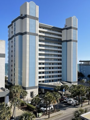 A multi-story hotel with a modern design, featuring a central atrium and a parking area with several cars. - The Soaring Seahaven (Myrtle Beach)