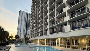 A high-rise hotel with a swimming pool, outdoor seating, and a clear view of the sunset. - The Soaring Seahaven (Myrtle Beach)