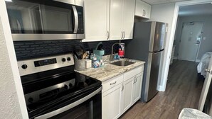 Una cocina con gabinetes blancos, un refrigerador de acero inoxidable, un microondas, una estufa y un lavamanos.