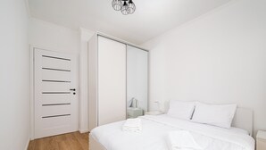 A bedroom with a bed, white bedding, a bedside table, a nightstand, a mirror, and a wardrobe. - Praga Południe Homely Apartment (Warszawa)