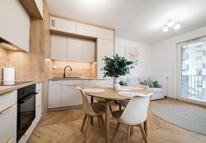 Una cucina moderna con mobili in legno, un tavolo da pranzo con sedie, una pianta in vaso e vista sulla città attraverso un'ampia finestra.