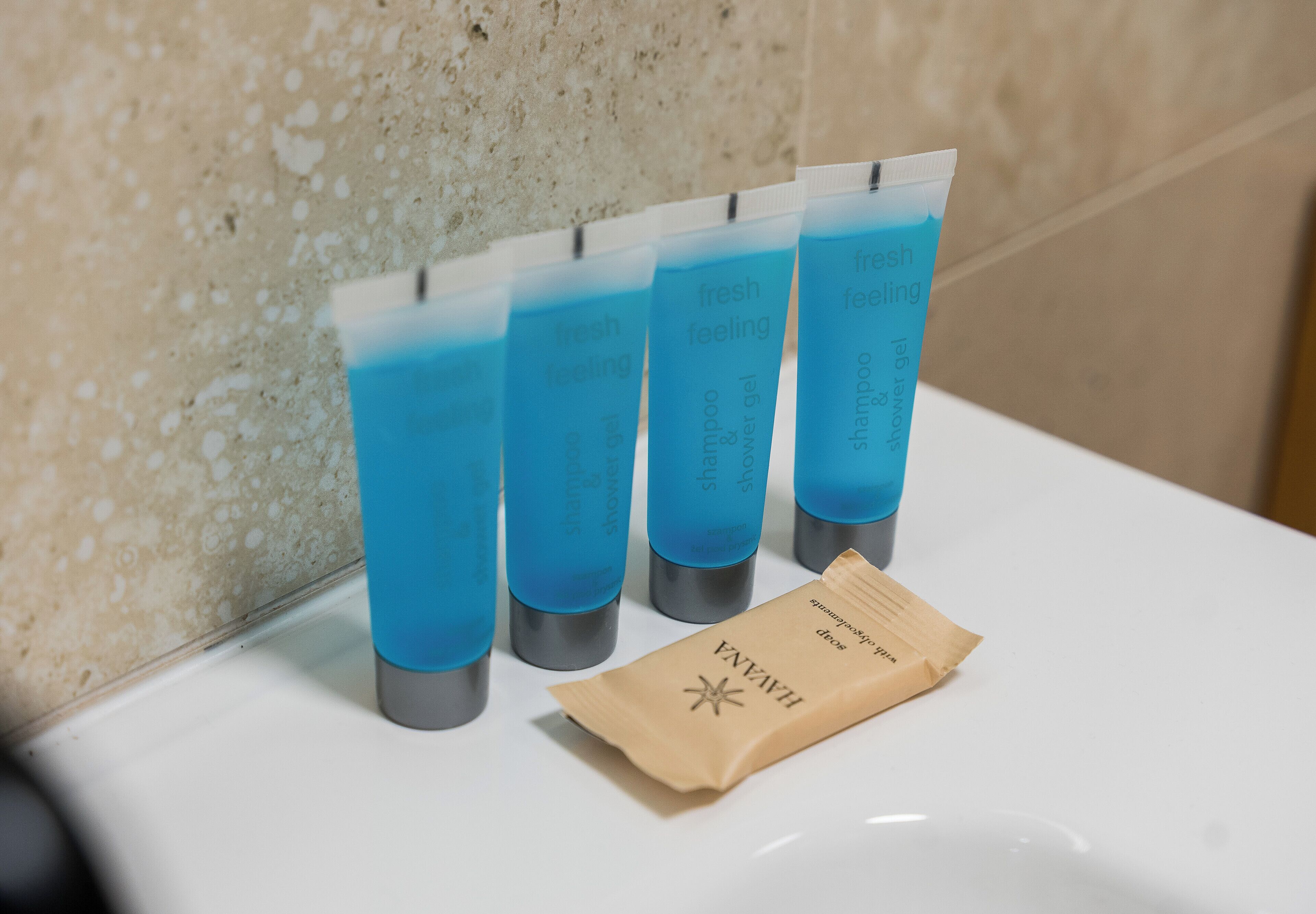 Un bagno con un lavandino, uno specchio e quattro flaconi blu di shampoo e bagnoschiuma.