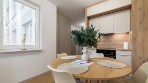 A dining area with a round wooden table, white chairs, and a potted plant. - Posnania Deluxe Apartment (Poznań)
