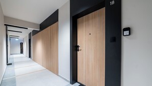 A hallway with a wooden door labeled "18", a black intercom, and a tiled floor. - Posnania Deluxe Apartment (Poznań)