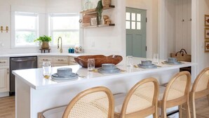 Une cuisine moderne avec des meubles blancs, un îlot central doté de sièges et un coin repas.