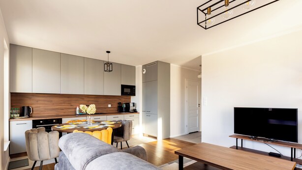 A modern living room with a grey sofa, a wooden dining table, and a flat-screen TV. - Starowiejska 91 Superior Apartment (Gdańsk)