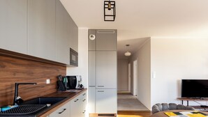 A modern kitchen with a built-in microwave, a coffee machine, and a sink. There is a wooden countertop and a chair in the dining area. - Starowiejska 91 Superior Apartment (Gdańsk)