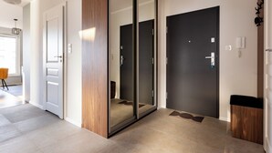 A modern hallway with a wooden door, a glass door, and a dark door. There is a light switch and a phone on the wall. - Starowiejska 91 Superior Apartment (Gdańsk)