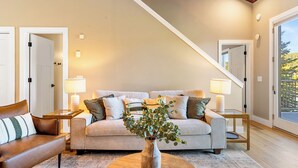 A living room with a sofa, a coffee table, and a vase with plants. There are two lamps on side tables, and a door is visible in the background. - NEW! Ski-In/Out, Lone Peak & Lake Views, 3B/3B (Big Sky)