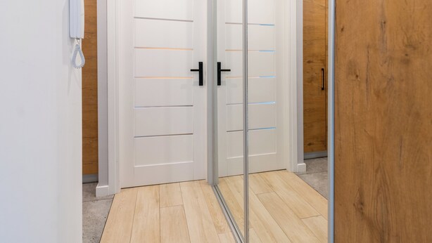 A hallway with two white doors, one with a phone on the wall, and wooden flooring. - Fabryczna City Apartment (Katowice)