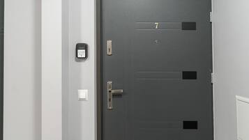 A dark grey door with a keypad lock, a doorbell, and a light switch on the wall beside it.