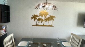 A dining area with a table set for four, white chairs, and a wall mural of palm trees. - PALM TREE PARADISE/PRIME LOCATION (Myrtle Beach)