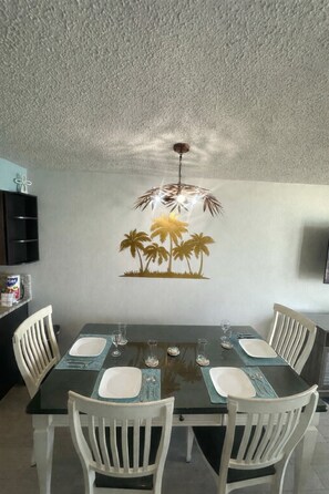 A dining area with a table set for four, white chairs, and a wall mural of palm trees. - PALM TREE PARADISE/PRIME LOCATION (Myrtle Beach)