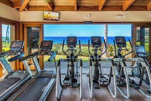 Un gimnasio con cintas de correr y elípticas, con vistas panorámicas al océano.