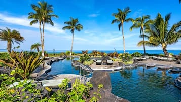 A pool area with palm trees and a view of the ocean.