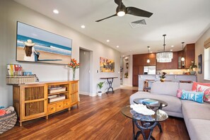 Una sala de estar moderna con un sofá, una mesa de centro, un aparador de madera y un cuadro con una escena de playa.