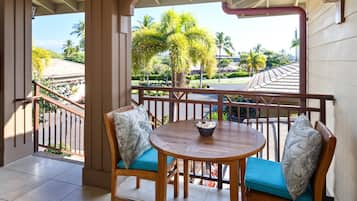 A covered outdoor seating area with a round table and two chairs, a railing, and a view of palm trees and buildings.