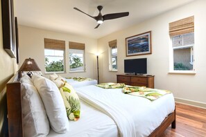 A bedroom with two beds, a ceiling fan, a TV, and windows with views of palm trees. - Halii Kai | Ocean View 4 BR, Sleeps 12 | Car Incl. w/ 6+ Nights | HLI ML-2567 by KBM (Waikoloa)