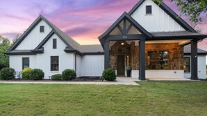 A modern two-story house with a stone facade, a covered porch, and a well-maintained lawn. - The Oakwood Villa - Ultimate Texas 4 BR Ranch with Pool 35 min to AT&T Stadium (Mansfield)