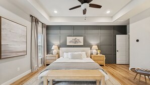 A bedroom with a bed, bedside tables, a ceiling fan, a door, and a window with curtains. - The Oakwood Villa - Ultimate Texas 4 BR Ranch with Pool 35 min to AT&T Stadium (Mansfield)