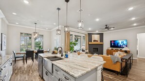 A spacious kitchen with a marble island, modern pendant lights, and a dining area with a wooden table and chairs. - The Oakwood Villa - Ultimate Texas 4 BR Ranch with Pool 35 min to AT&T Stadium (Mansfield)