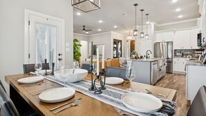 A modern dining room with a wooden table set for six, white plates, and candles. - The Oakwood Villa - Ultimate Texas 4 BR Ranch with Pool 35 min to AT&T Stadium (Mansfield)