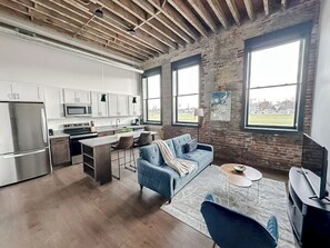 Una cocina moderna con electrodomésticos de acero inoxidable, un comedor con un sofá azul y ventanas amplias con vistas.