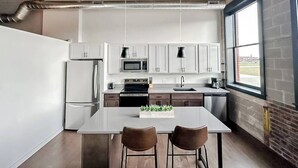 A modern kitchen with white cabinets, stainless steel appliances, and a large island with two chairs. - Sleepover | Stylish 1BD/1BA Loft - Newton (Newton)