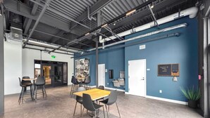 A conference room with a wooden table and black chairs, a blue accent wall, and visible ceiling pipes. - Sleepover | Stylish 1BD/1BA Loft - Newton (Newton)