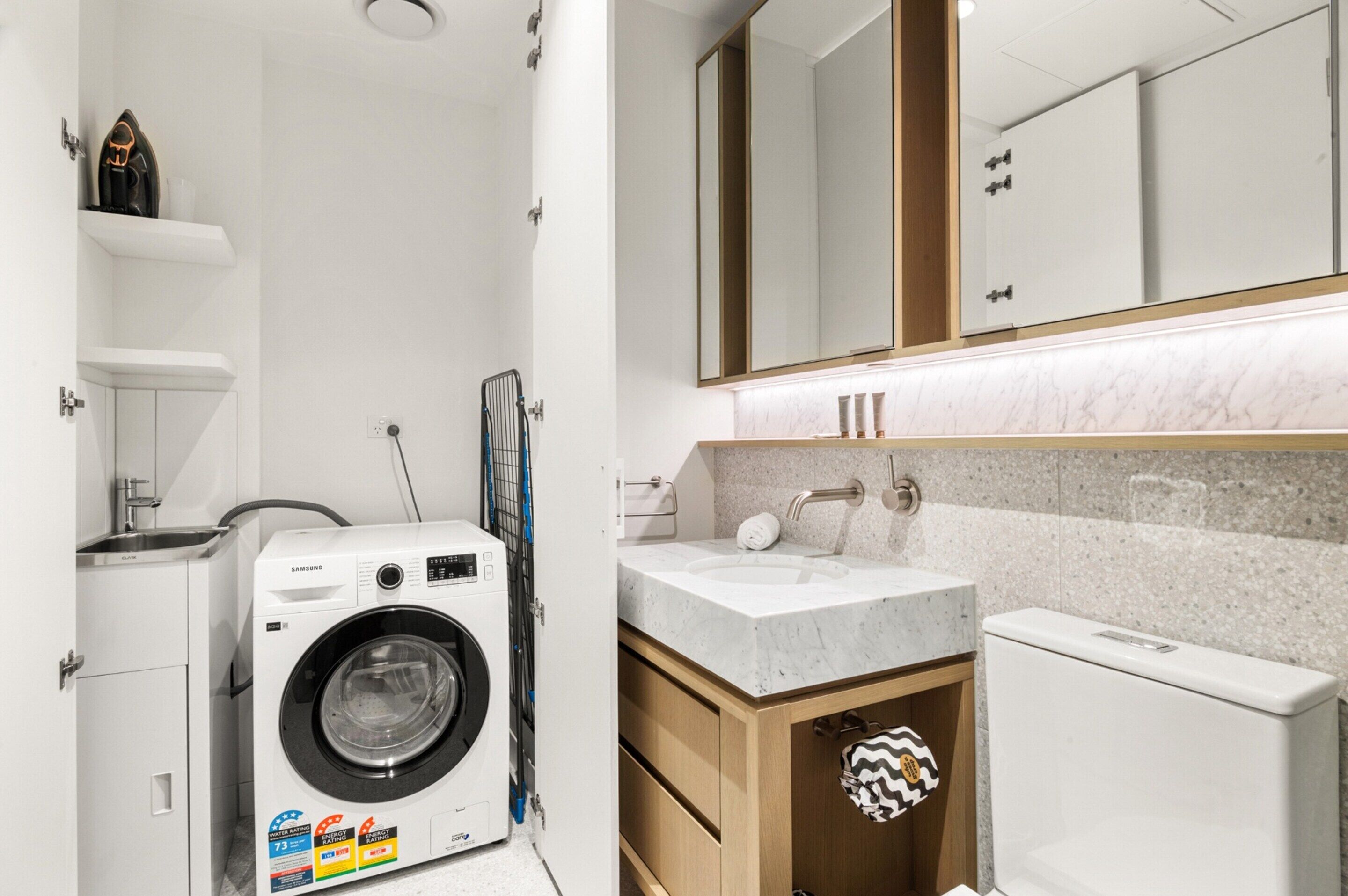 A modern bathroom with a built-in washing machine, a sink, and a large mirror.