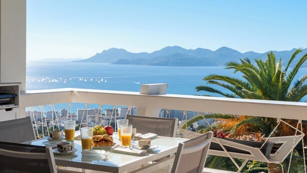 A balcony with a table set for breakfast, overlooking a coastal view with mountains and the sea. - 2-Br Panoramic Views – Top Floor, Cannes (Cannes)